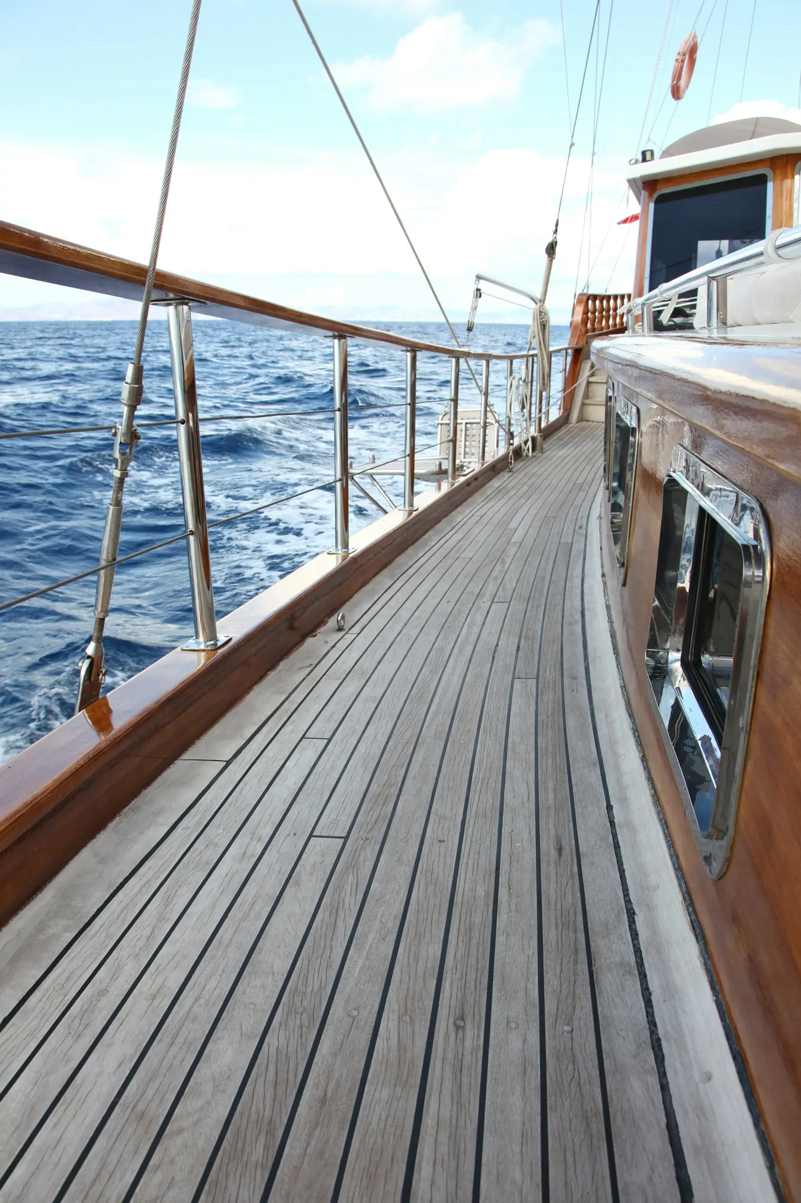 Varnished teak side deck of a sailing yacht underway, open sea beyond the rail