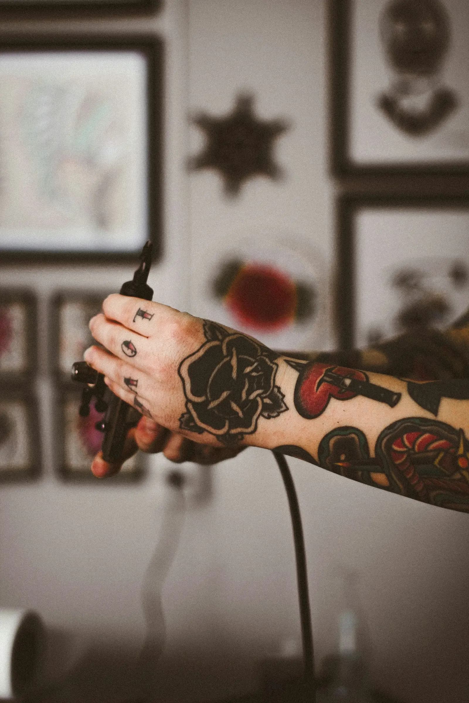 Tattooed hand holding a machine in front of a wall of framed flash art