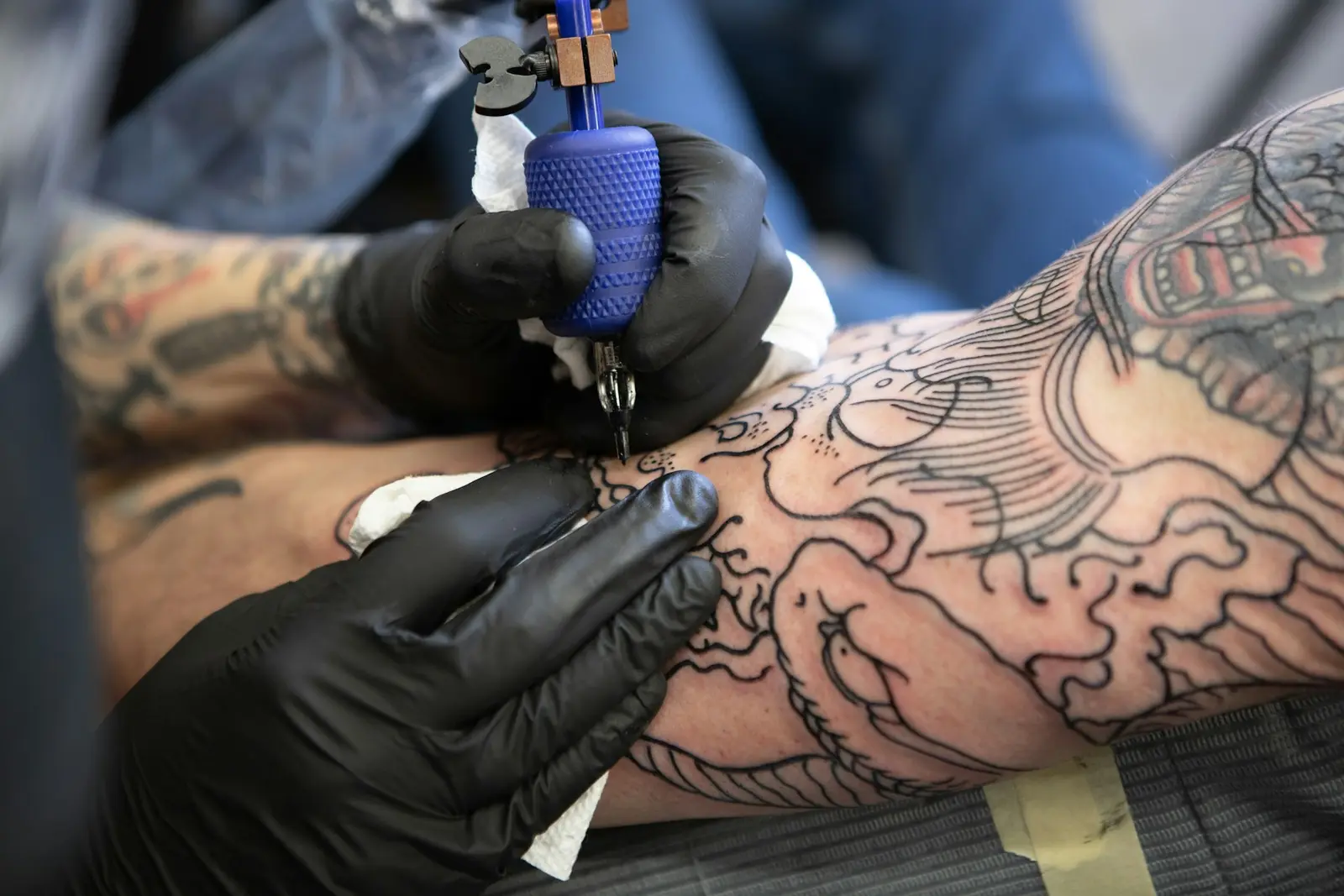 Gloved hands lining a fresh outline on a tattooed arm