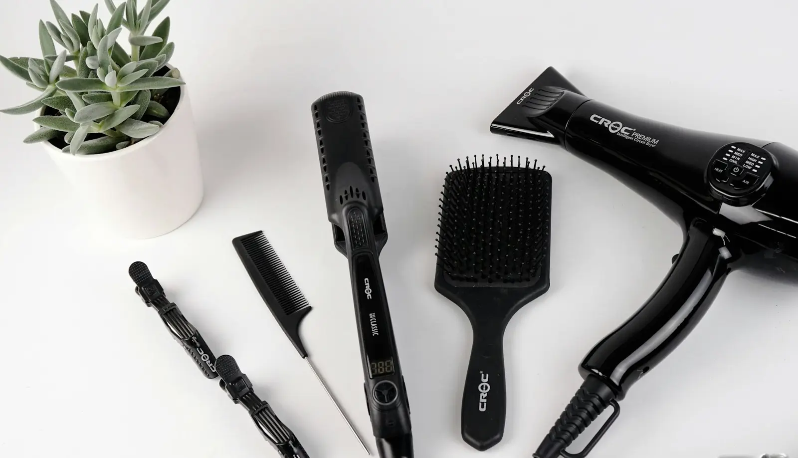 Stylist's kit — dryer, paddle brush, straightener, combs and clips laid out on white