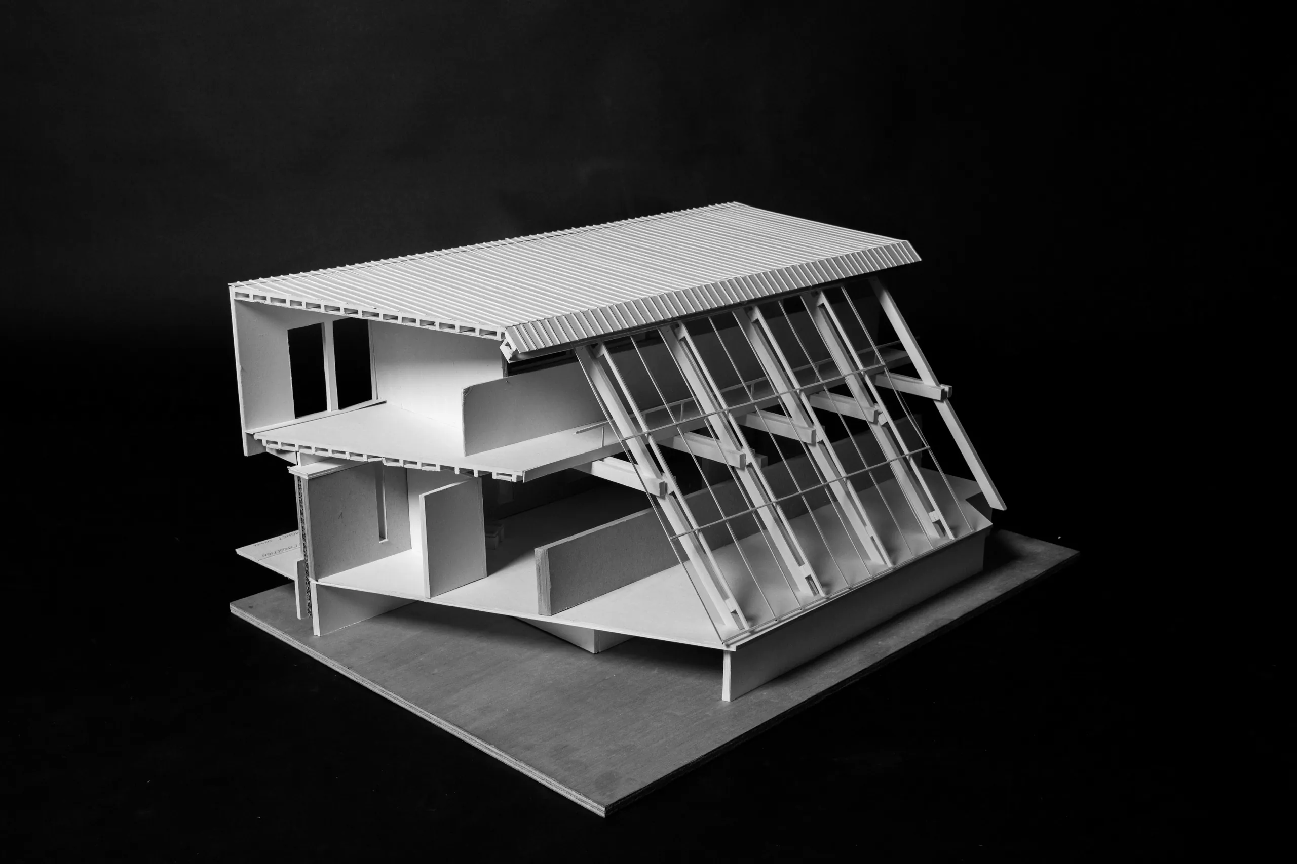 Monochrome photograph of a sectional card model on a dark ground: two floor plates, a raking roof and fine card rafters