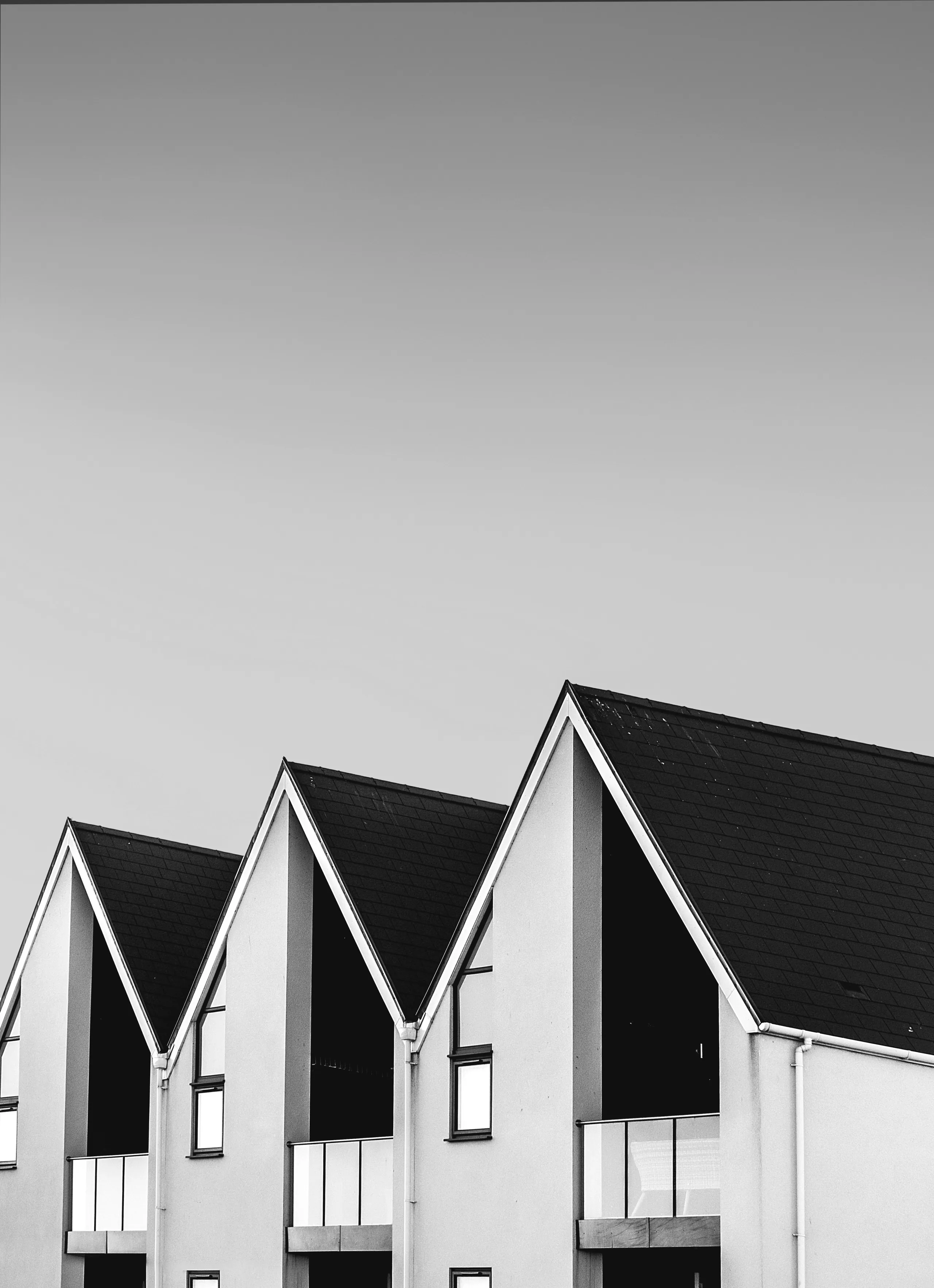 Monochrome photograph of three identical gable ends in a row against an empty sky, each with a deep recessed loggia under the roof pitch