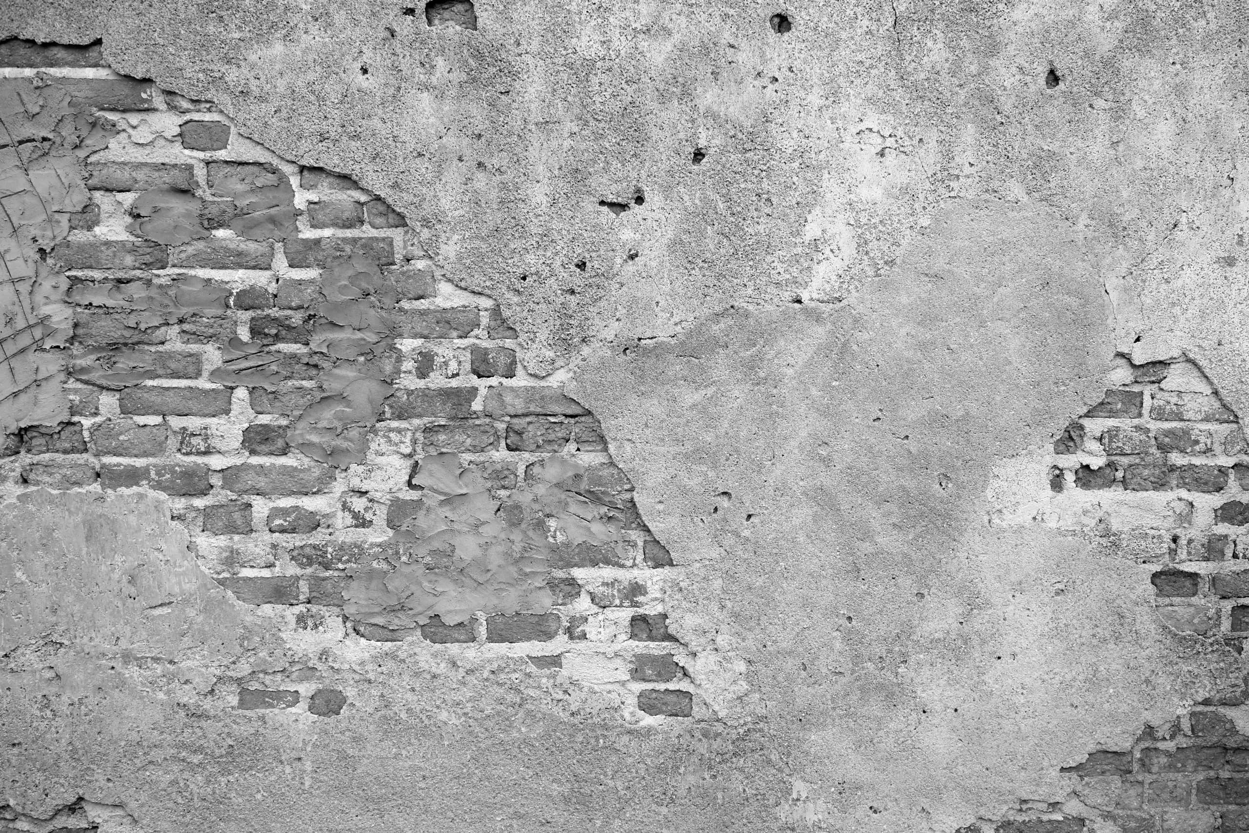 Monochrome detail of soft brick exposed where cement render has broken away