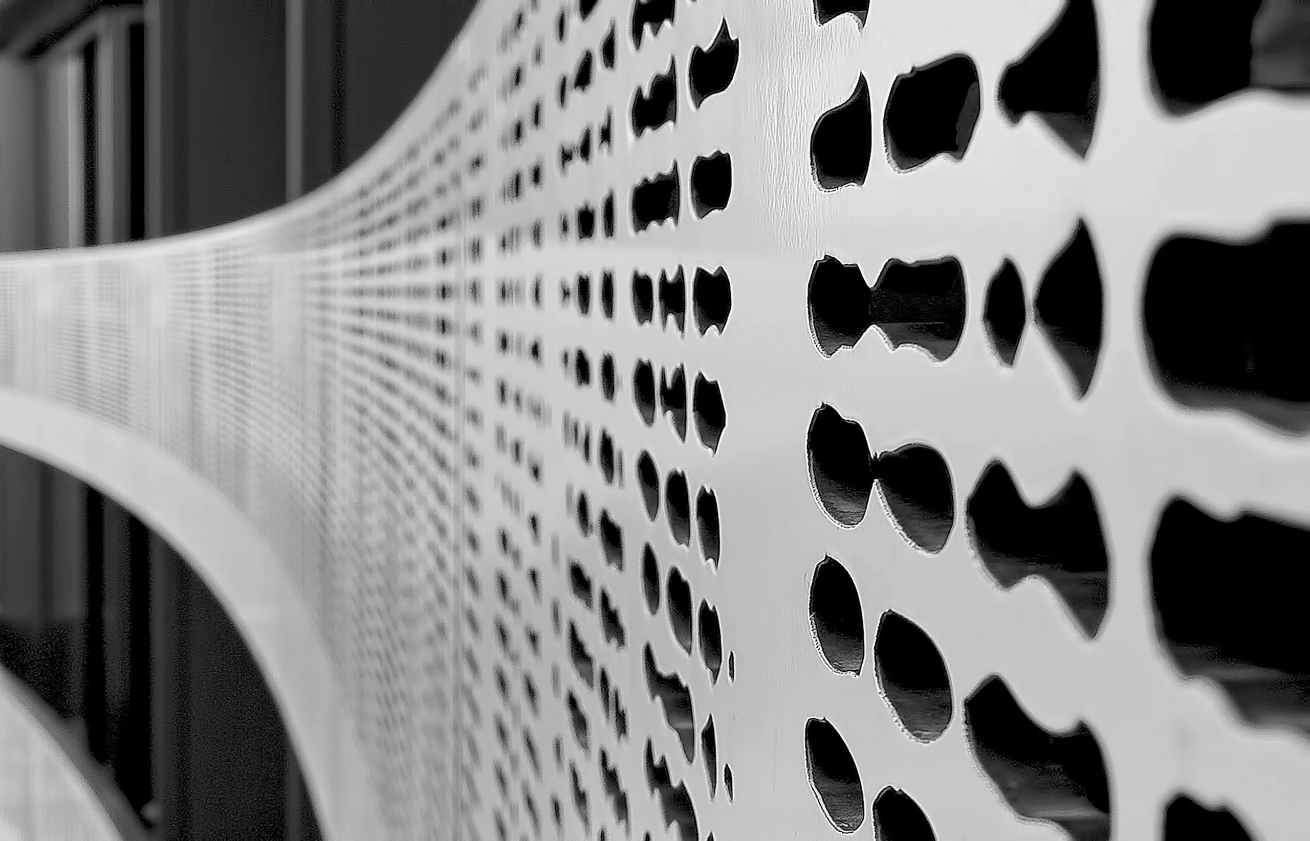 Monochrome detail of a perforated white metal screen at a raking angle