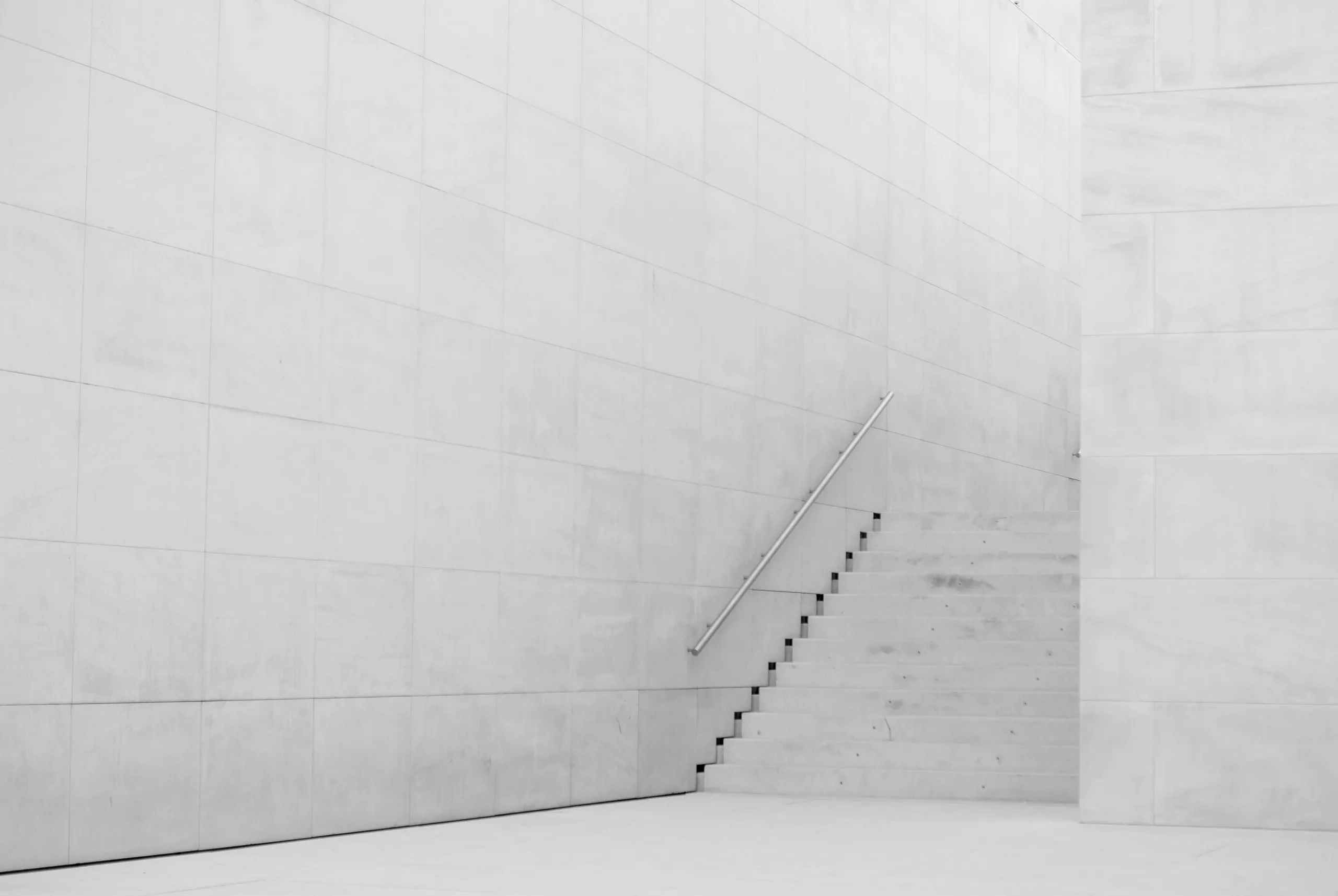 Monochrome detail of a pale concrete panel wall with a steel handrail