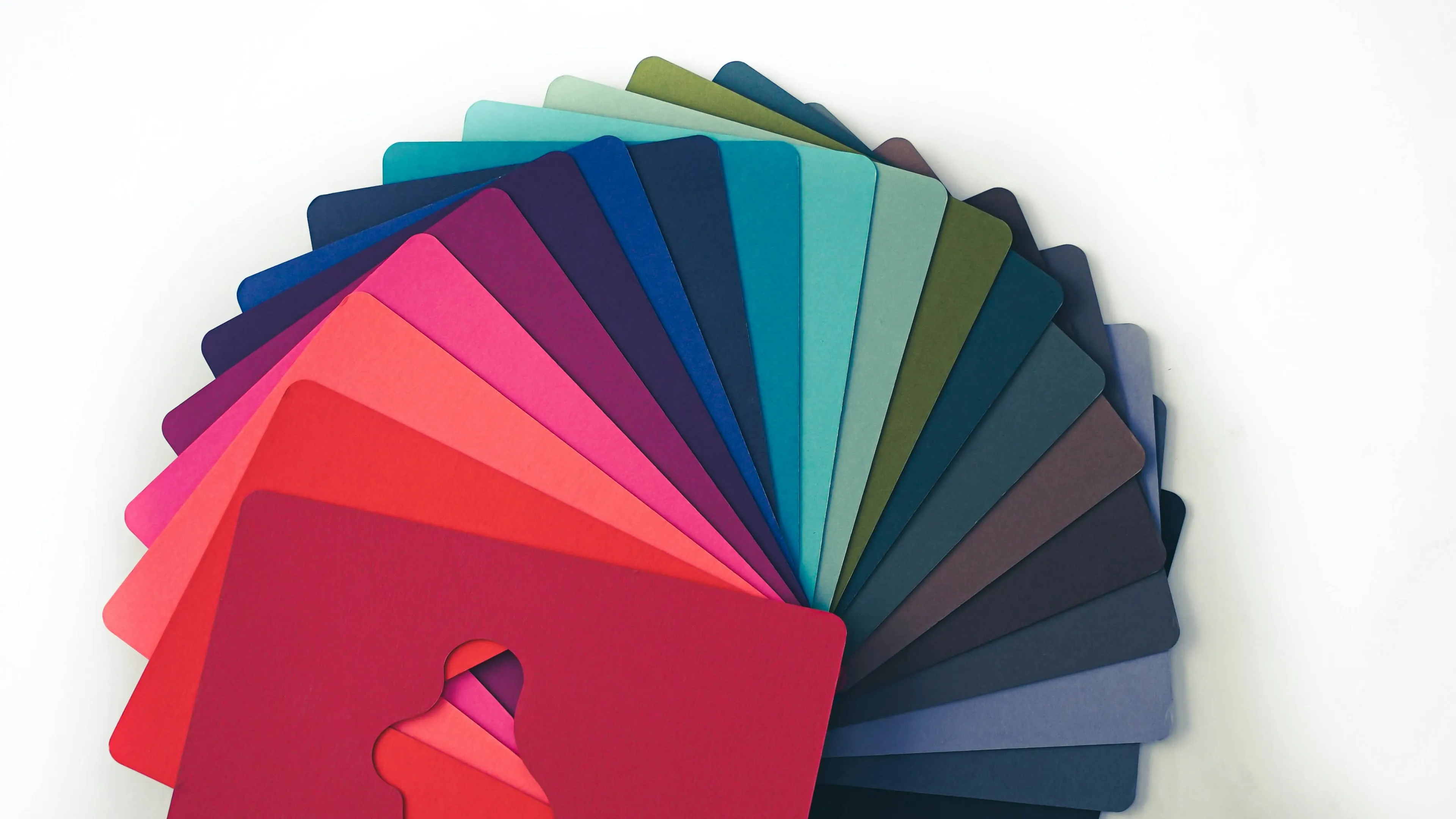 A fan of plain colour cards spread in an arc on a white surface, reds through blues and greens