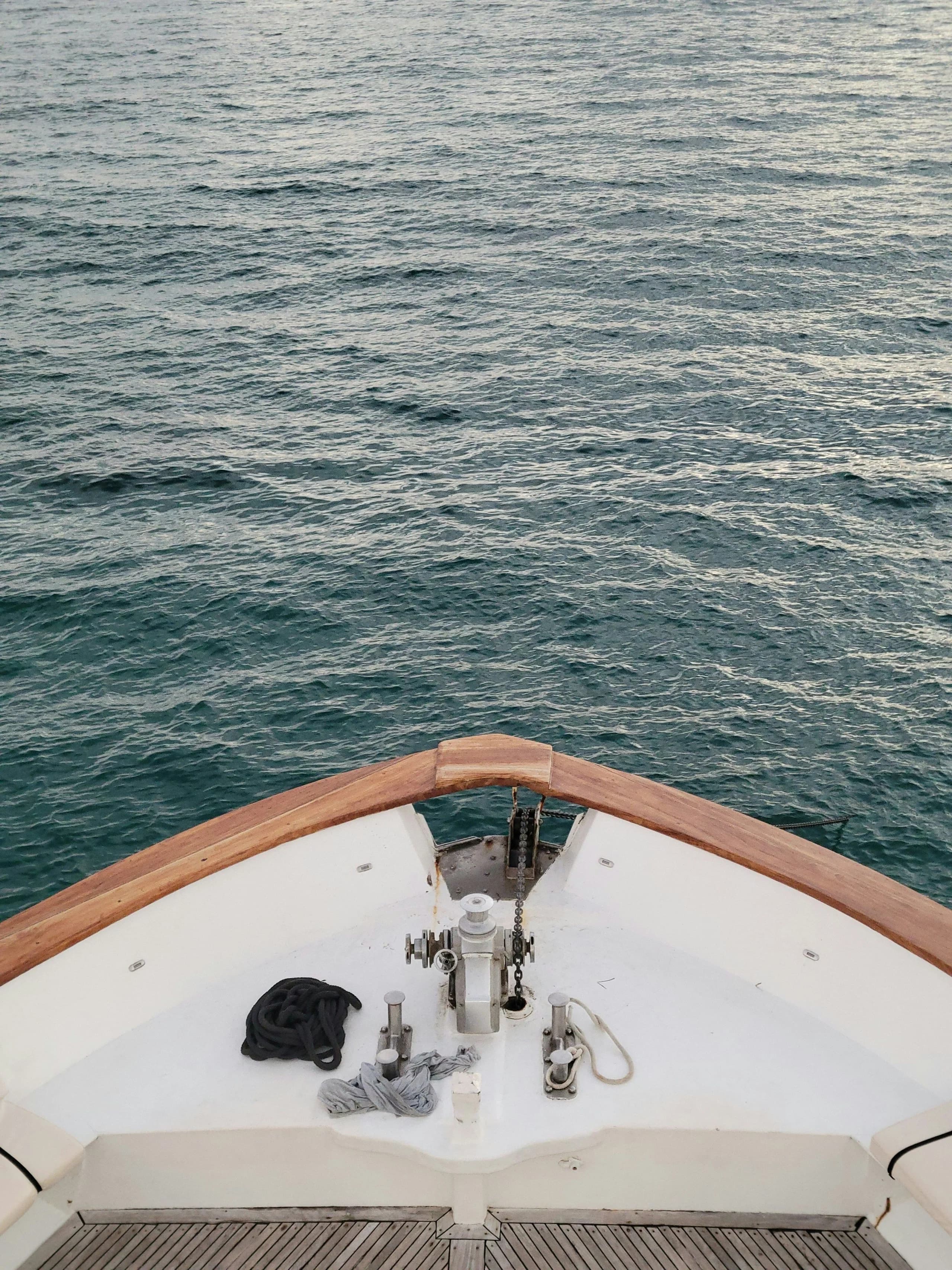 Looking down over the bow of a yacht at the anchor windlass and chain, dark water beyond