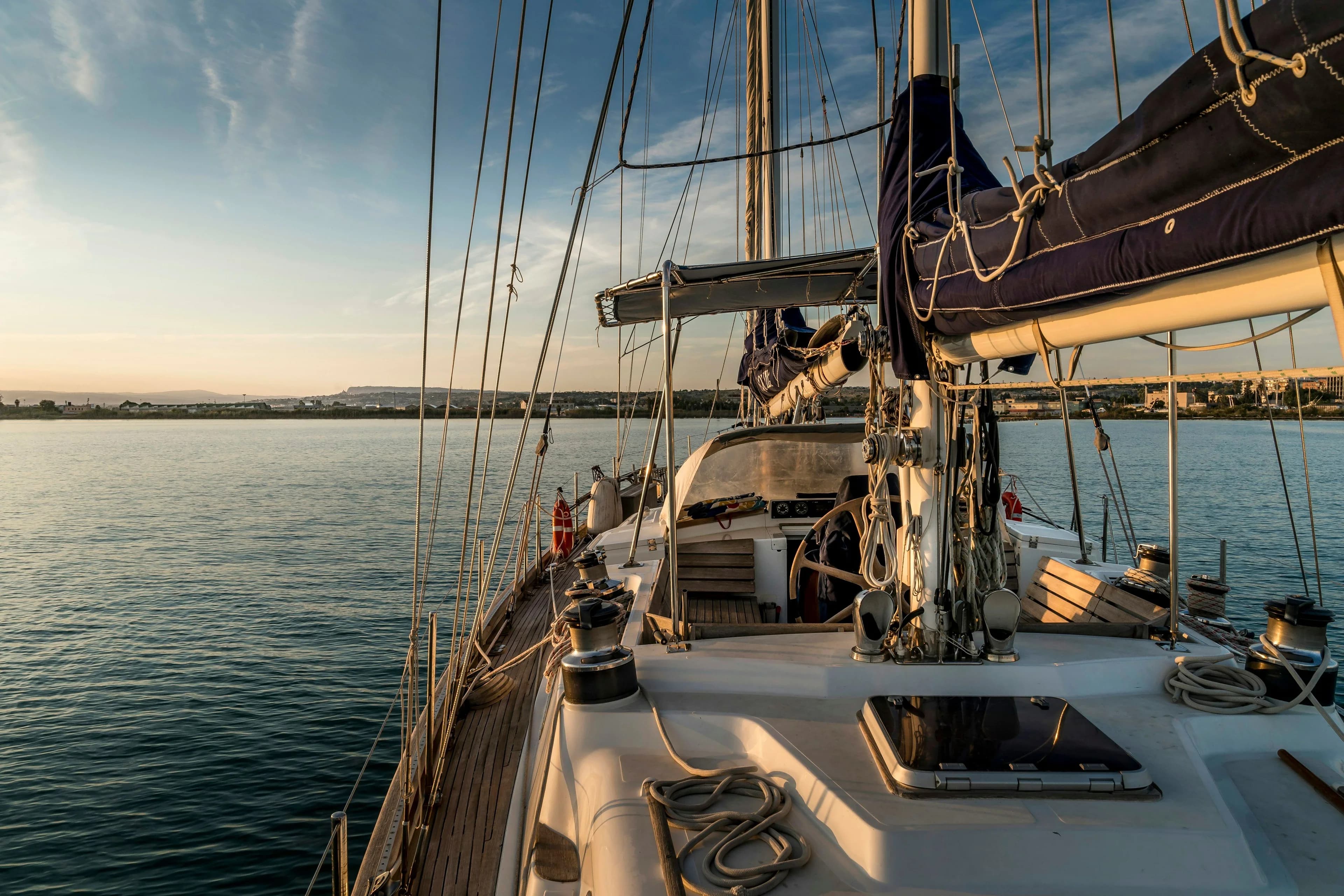 The teak side deck and winches of a large sloop at golden hour, coast low on the horizon