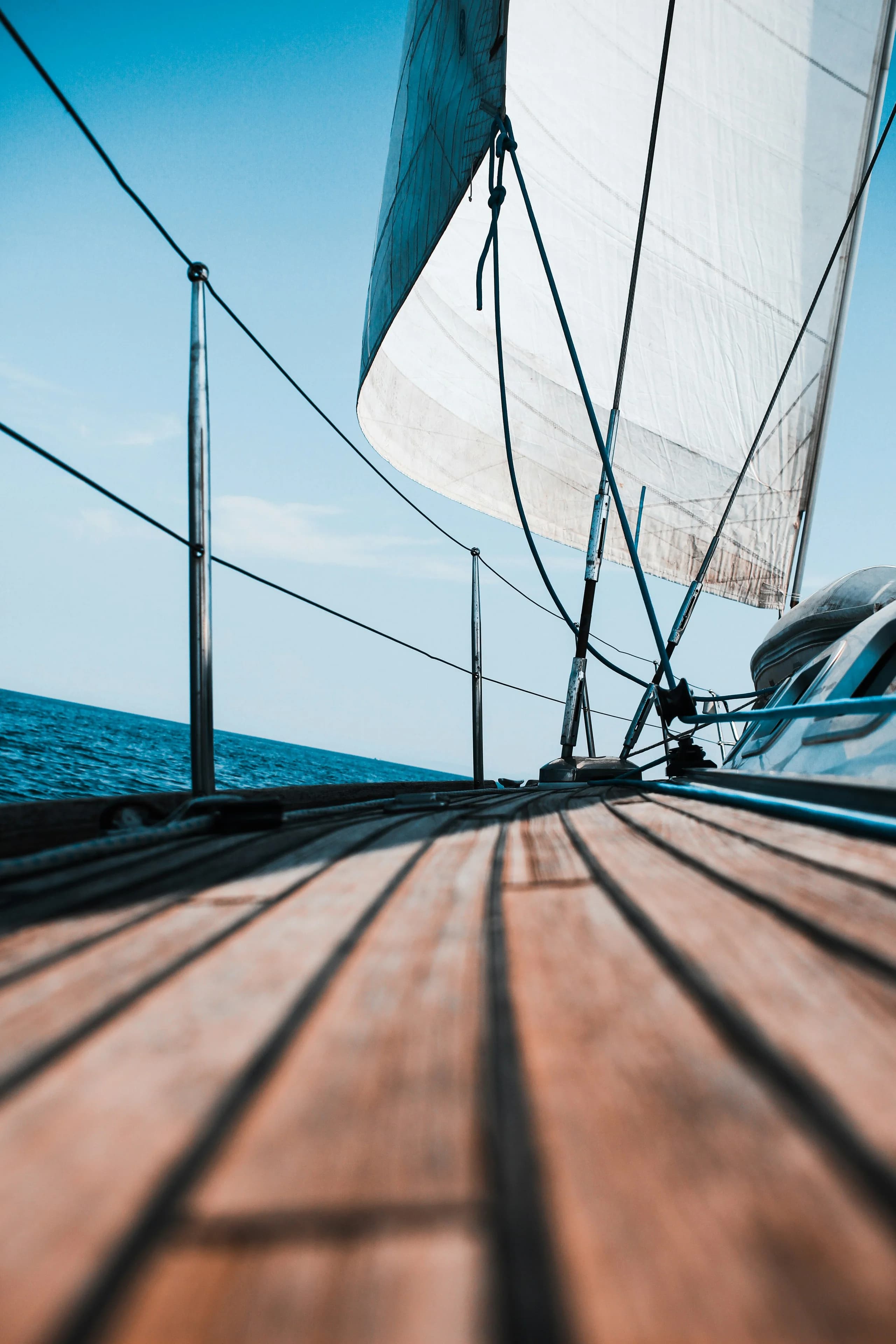 Low view along a varnished teak deck towards the headsail, open sea and a clear horizon ahead
