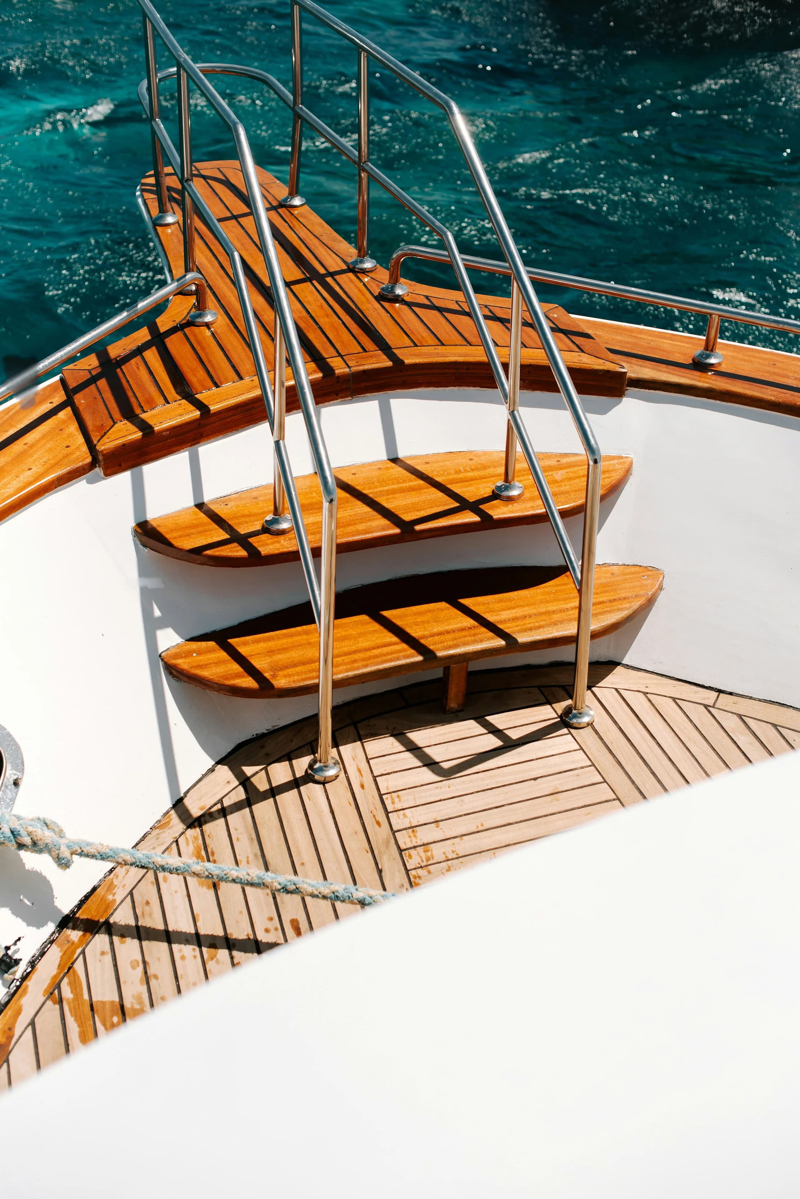 Varnished boarding steps and a stainless handrail at the side of a yacht, clear water below