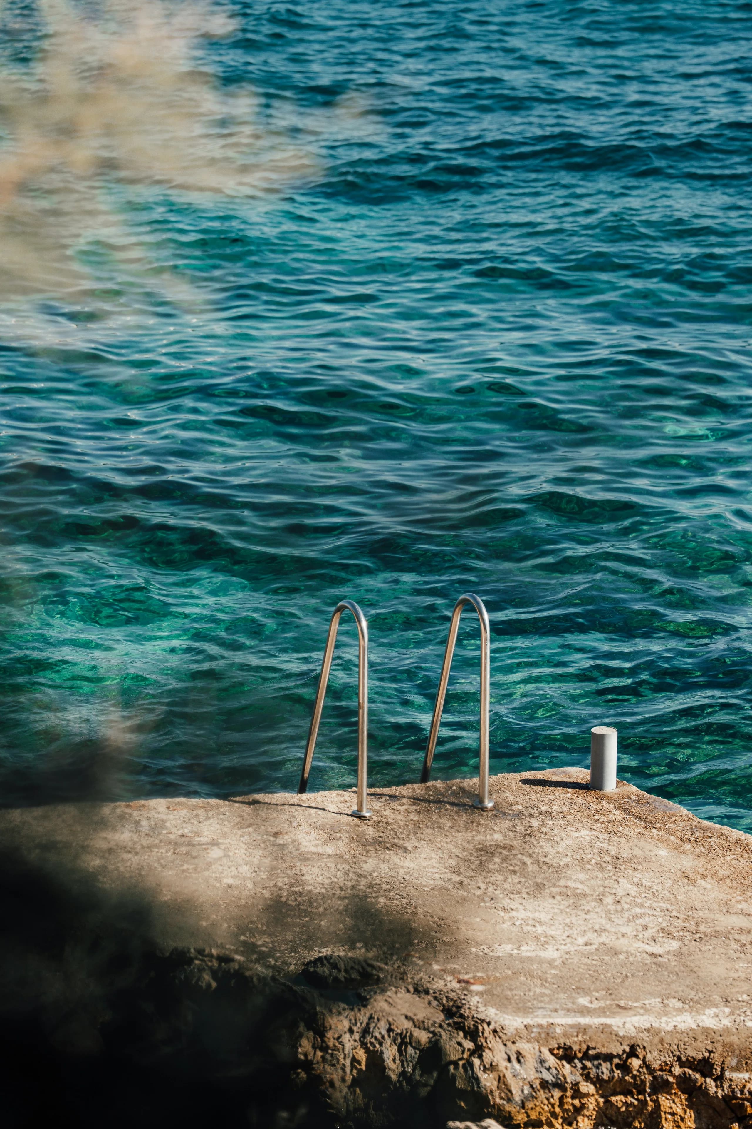 A stainless bathing ladder set into a limestone ledge, dropping into clear green-blue water